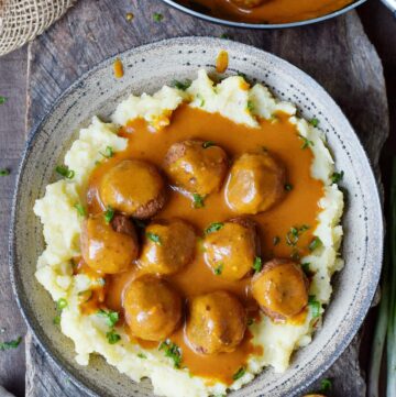 vegan meatballs with gravy over mashed potatoes in large bowl