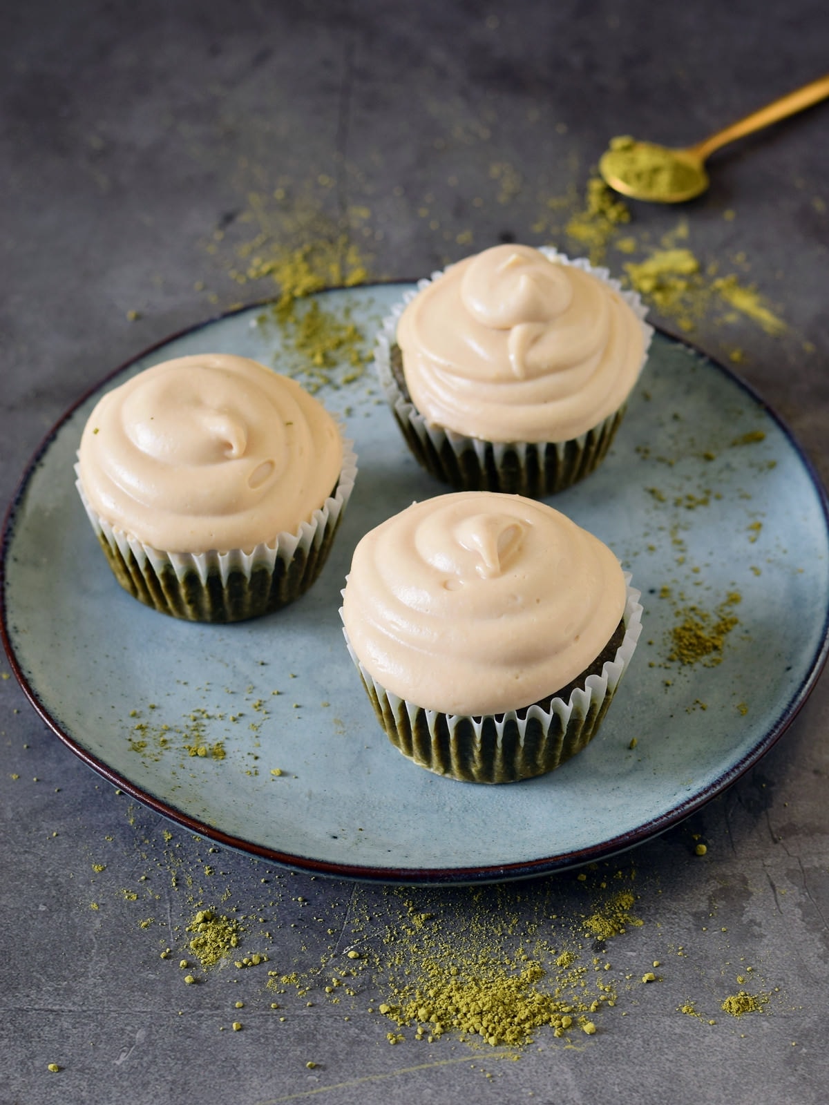 3 matcha cupcakes with white cashew frosting on blue plate