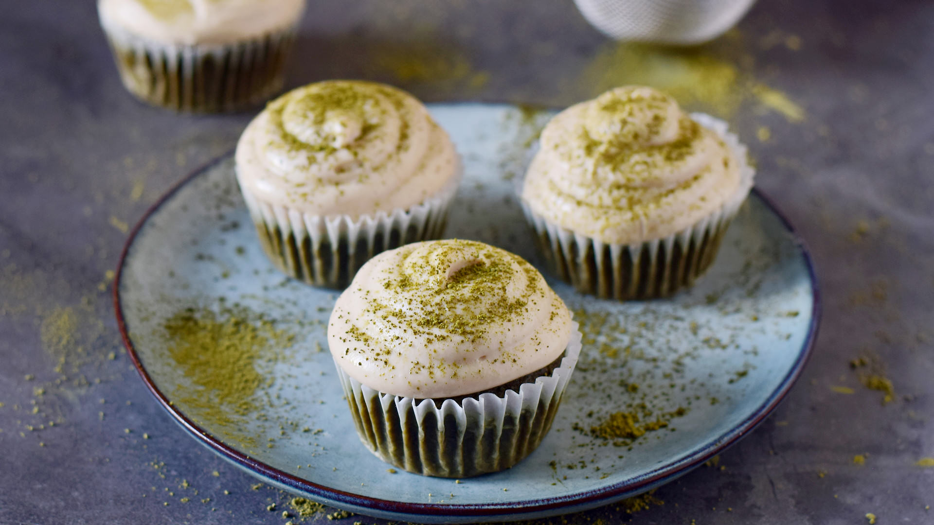 horizontal shot of 3 matcha cupcakes with white frosting on blue plate