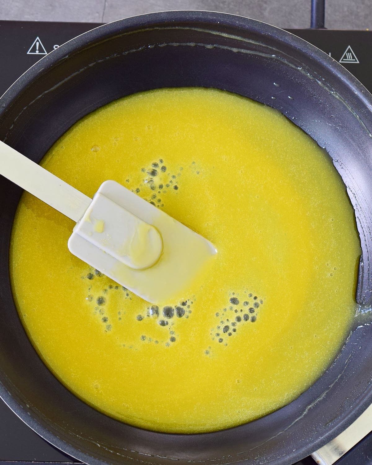 orange juice with agar powder in black skillet with spatula
