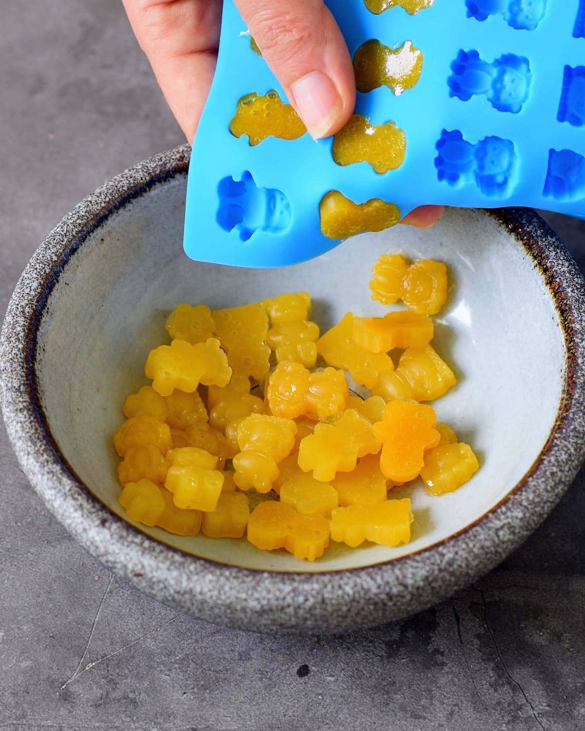 gelbe vegetarische Fruchtgummis werden aus blauer Silikonform in eine Schüssel gedrückt