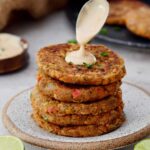 stack of lentil patties with spoon drizzling creamy white sauce on top