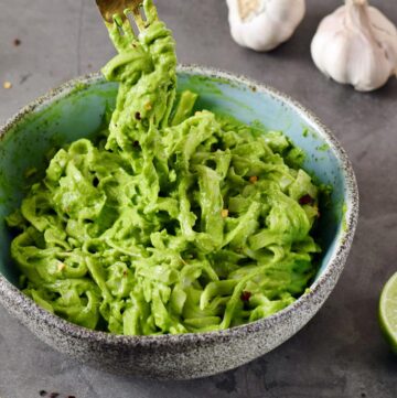 creamy green kale avocado pasta in blue bowl with fork