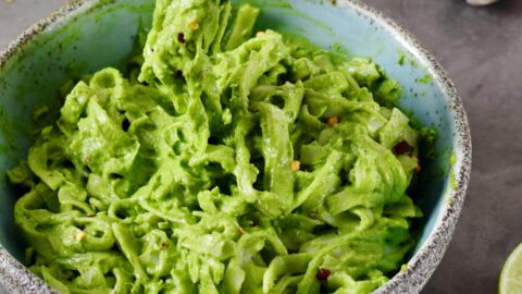 creamy green kale avocado pasta in blue bowl with fork