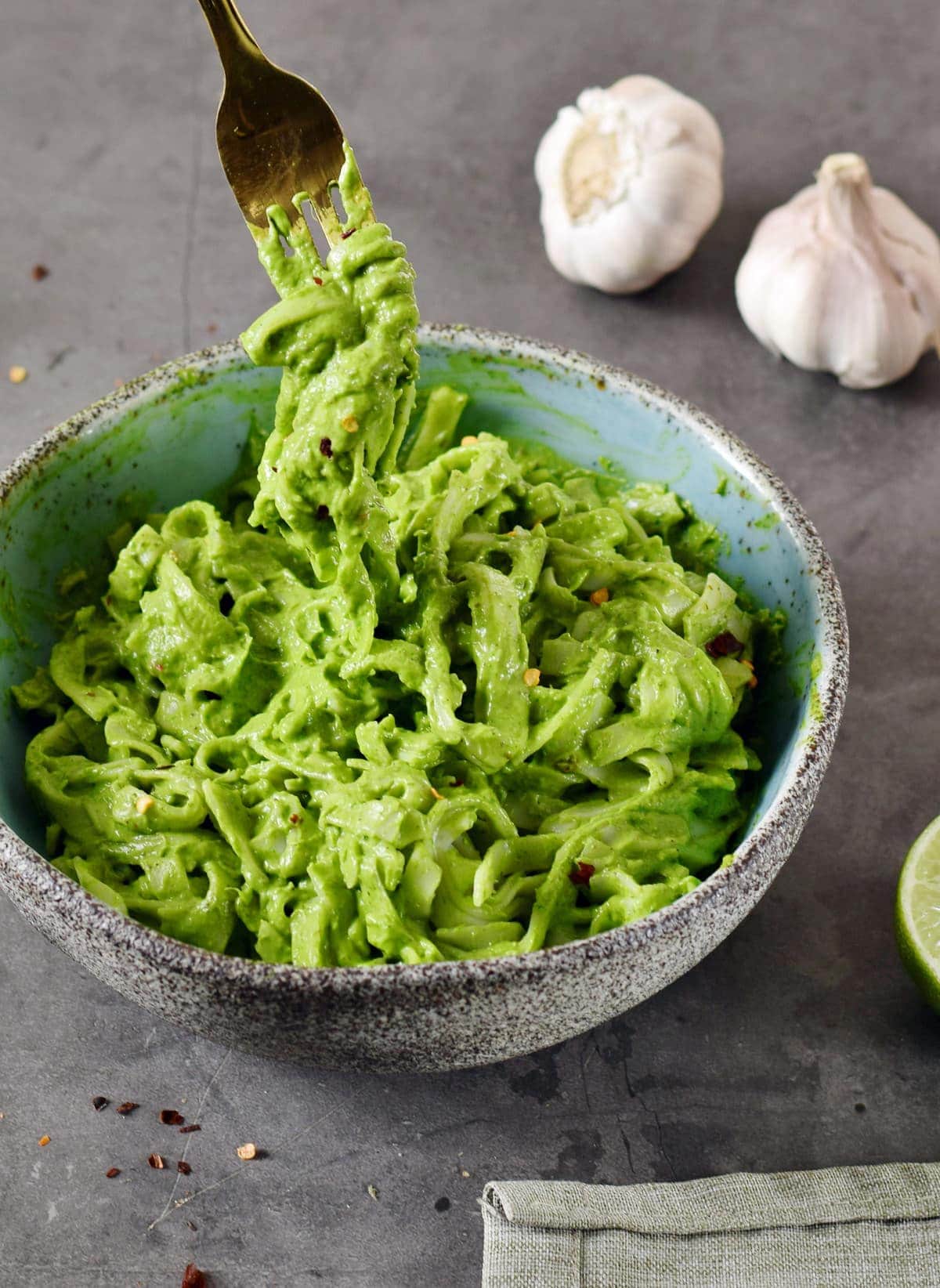 creamy green kale avocado pasta in blue bowl with fork