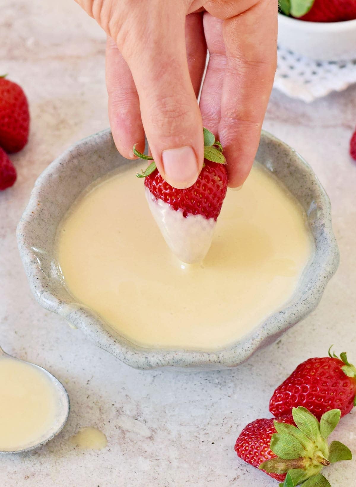 Hand taucht eine Erdbeere in eine Schüssel mit selbstgemachter süßer evaporated milk