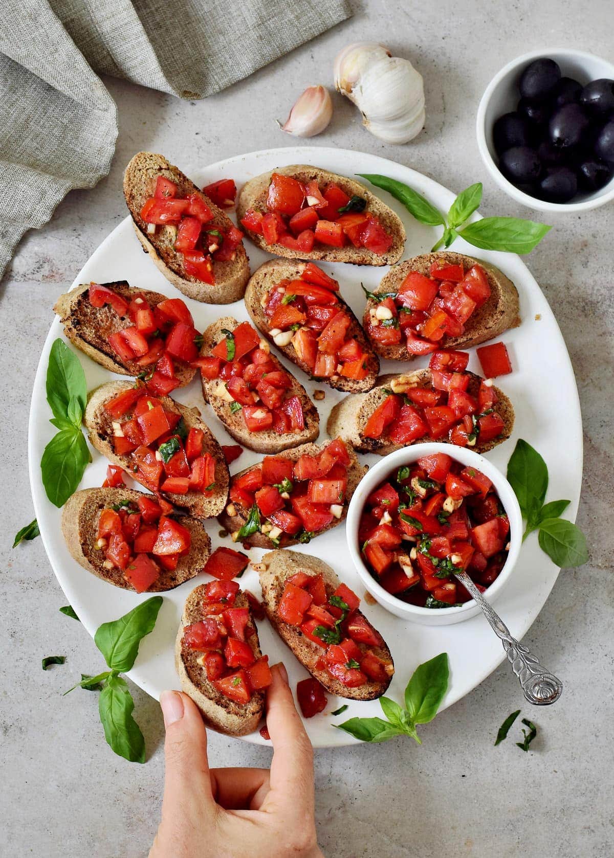 hand grabs a piece of homemade baguette topped with bruschetta on large white plate
