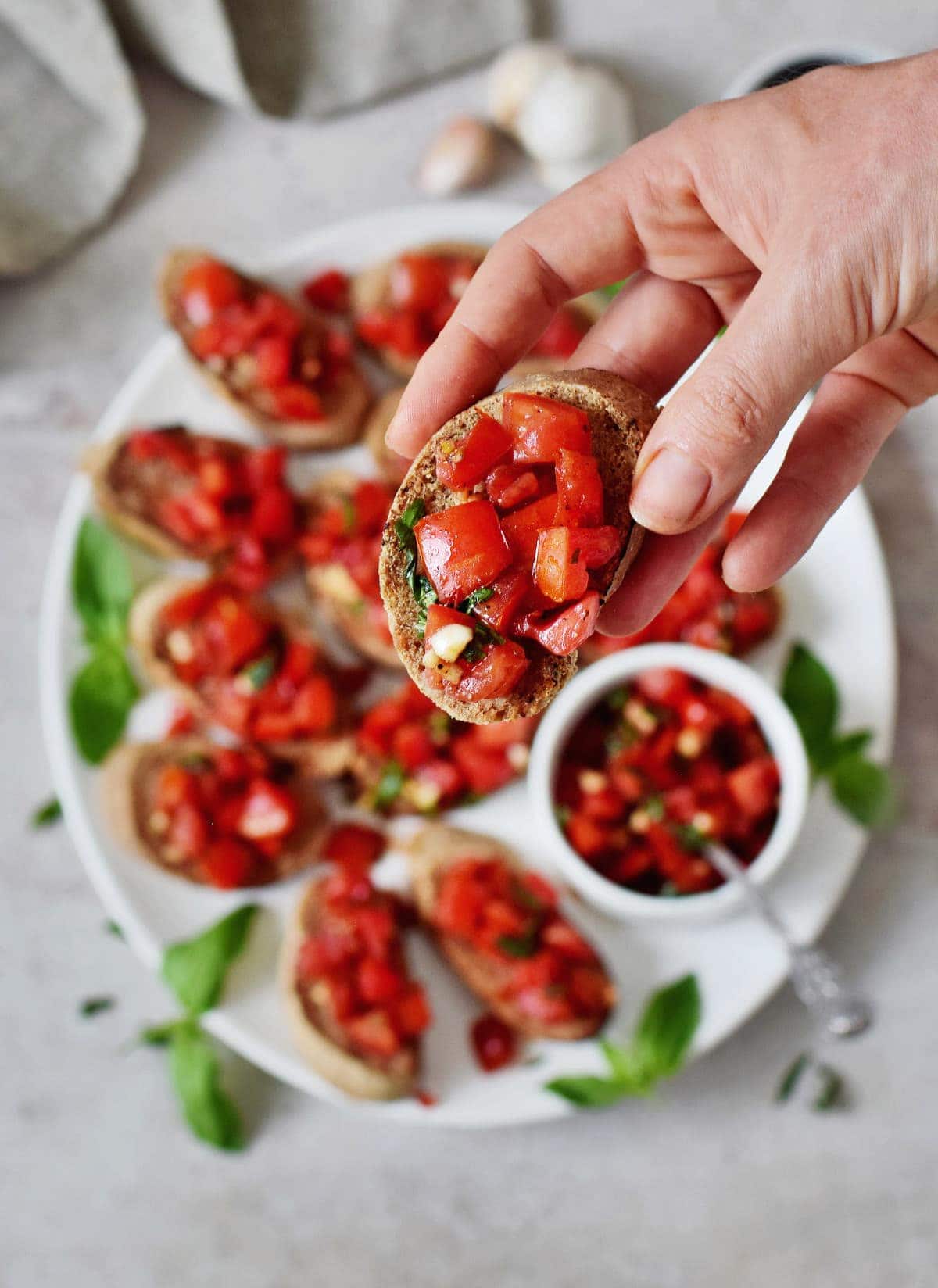 Hand hält ein Stück Baguette-Brot, belegt mit einer Tomaten-Basilikum-Knoblauch-Mischung