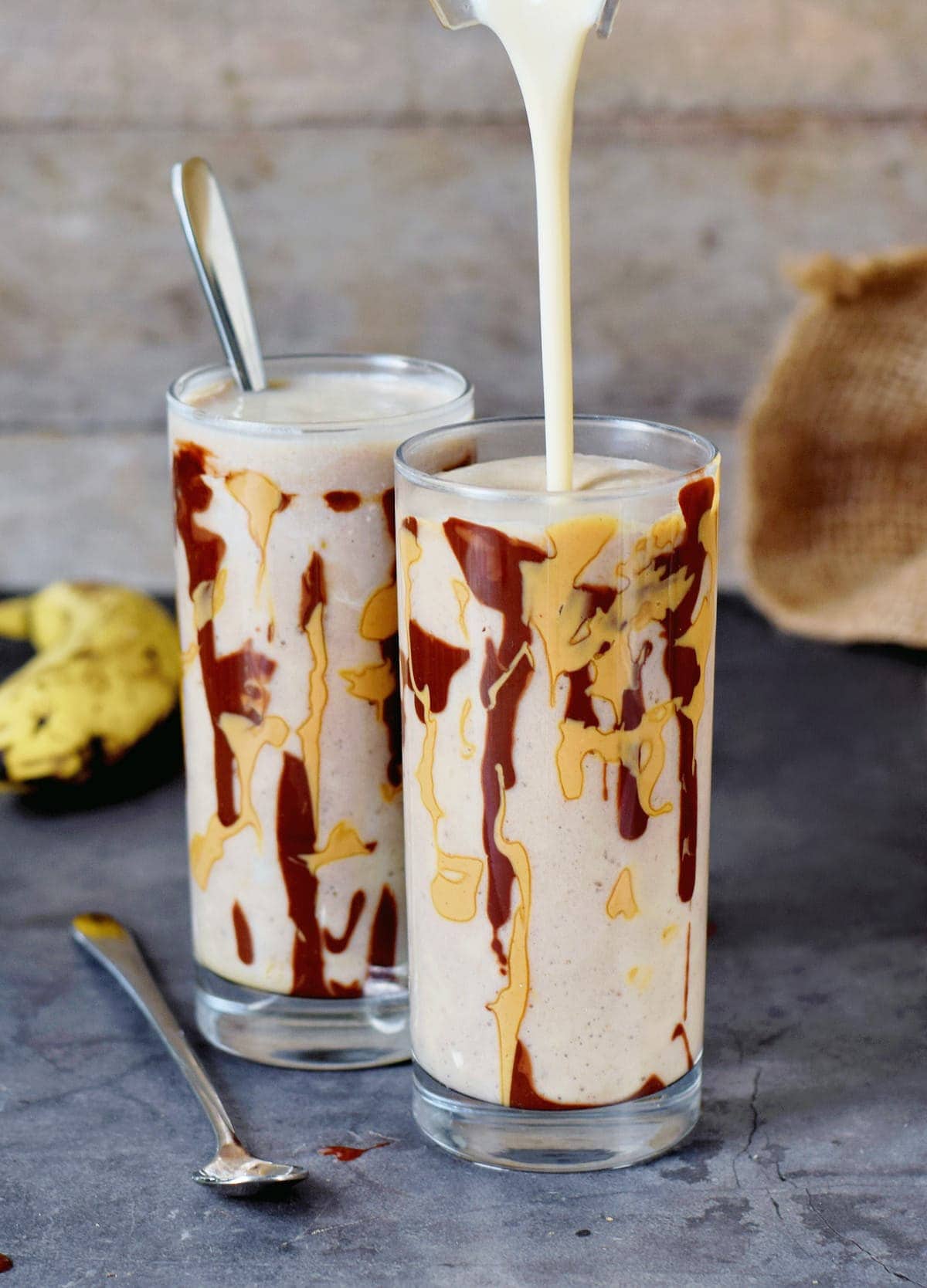 Bananen-Milchshake wird in ein Glas gefüllt welches mit Schokolade und Erdnussmus dekoriert ist