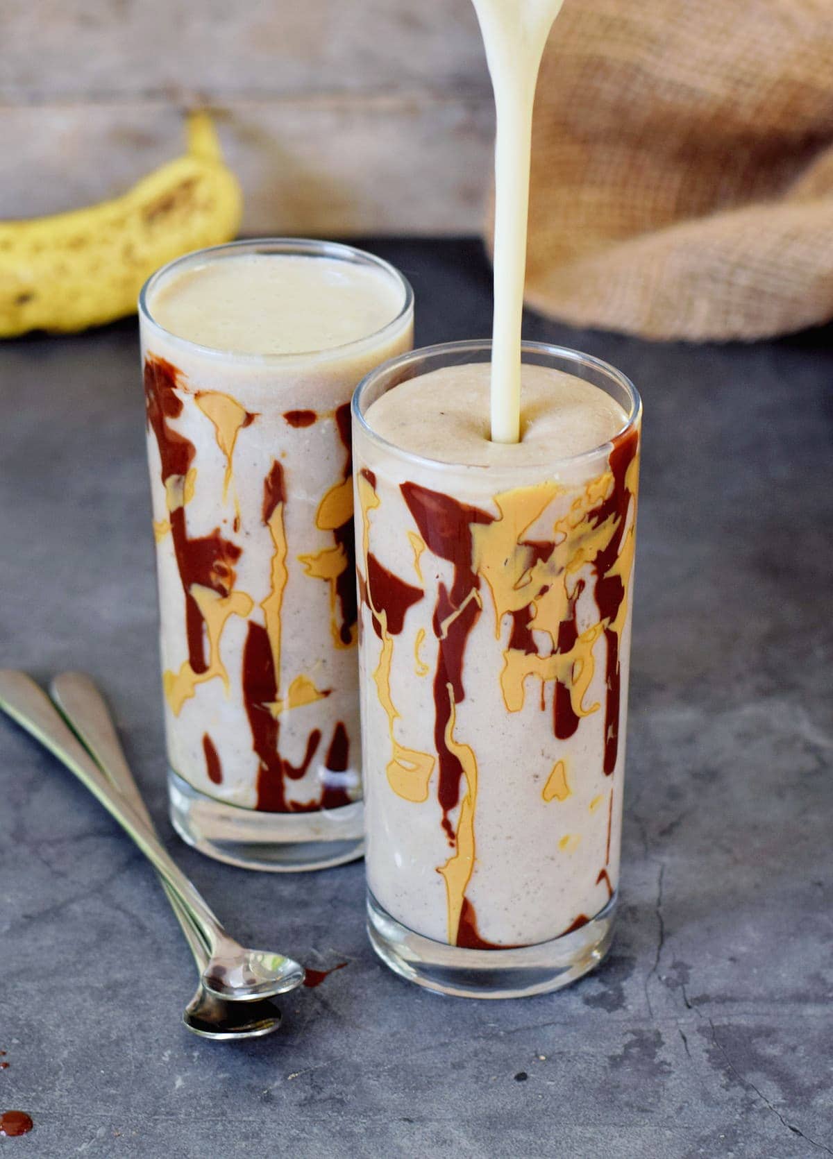 vegan banana milkshake in two glass jars with peanut butter chocolate drizzle