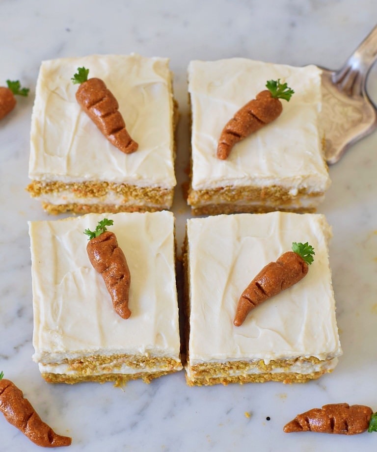 4 Stücke veganer Karottenkuchen von oben mit weißer Creme und Marzipan-Karotten darauf.