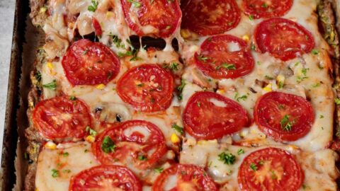 hand grabbing a piece of a keto zucchini pizza crust topped with tomatoes and vegan cheese