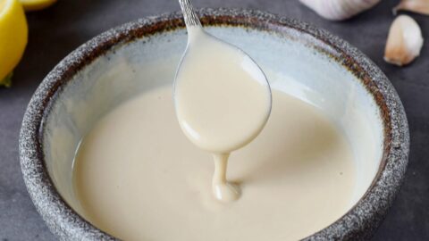 hand holding a spoon over a bowl filled with a tahini dressing