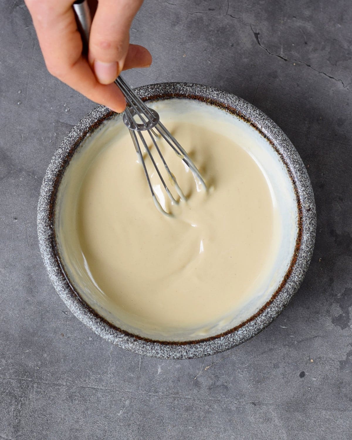 hand stirring tahini sauce in bowl with whisk
