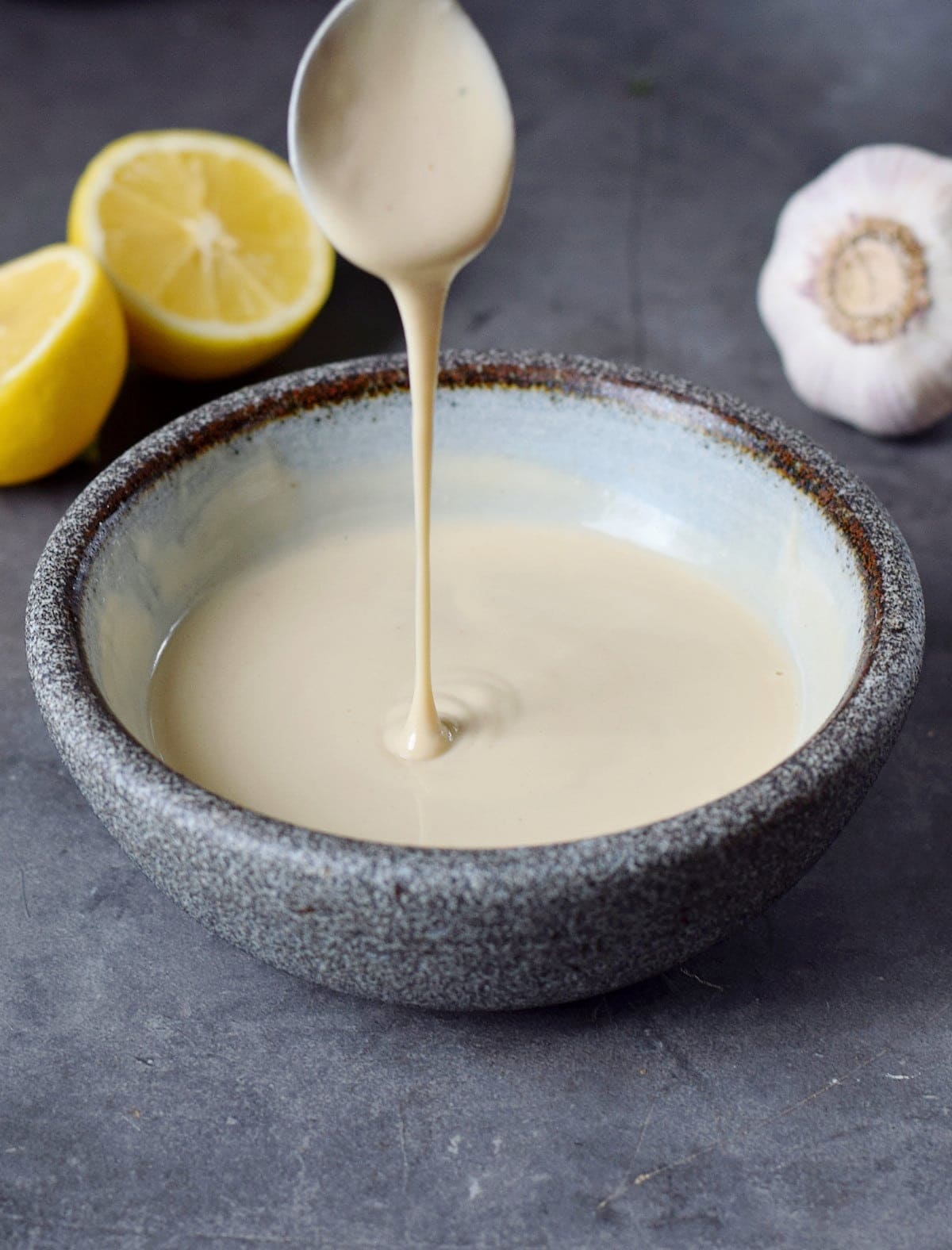 spoon with drizzle over tahini sauce in bowl