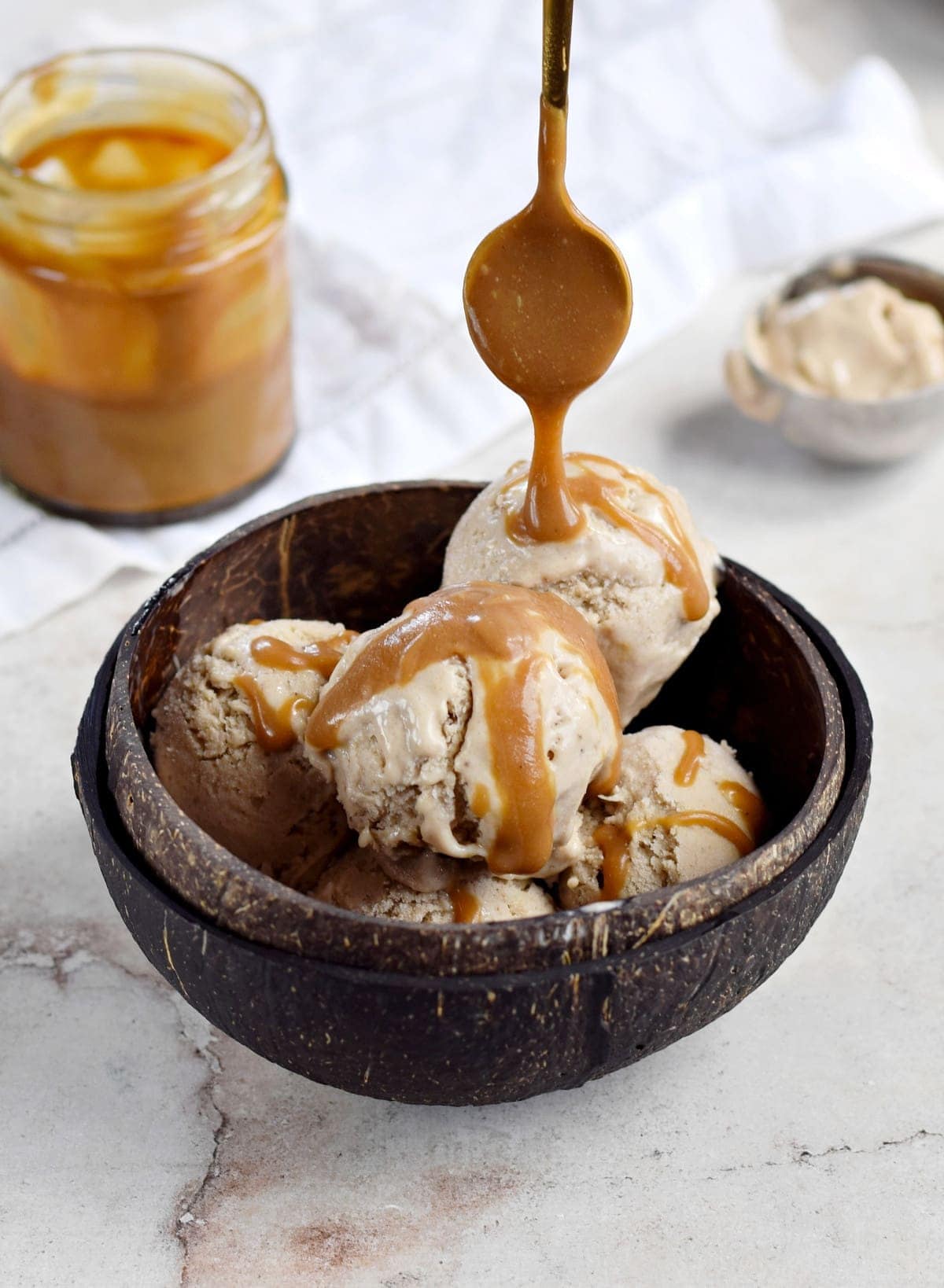 scoops of peanut butter banana ice cream in bowl with caramel sauce drizzle