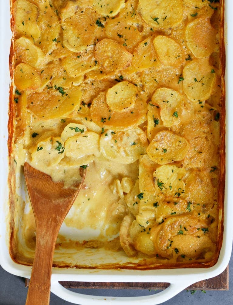 scalloped potatoes with wooden spoon in a baking dish