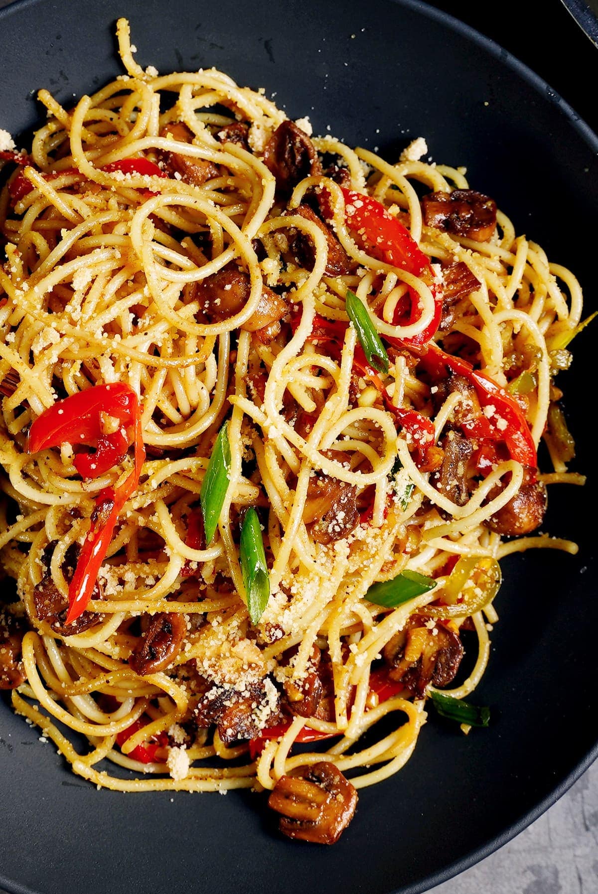 close-up of spaghetti aglio e olio with peppers and mushrooms in black bowl