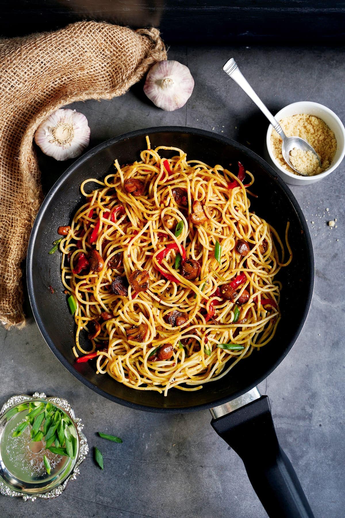 gebratene Knoblauchspaghetti mit Paprika und Champignons in schwarzer Pfanne von oben