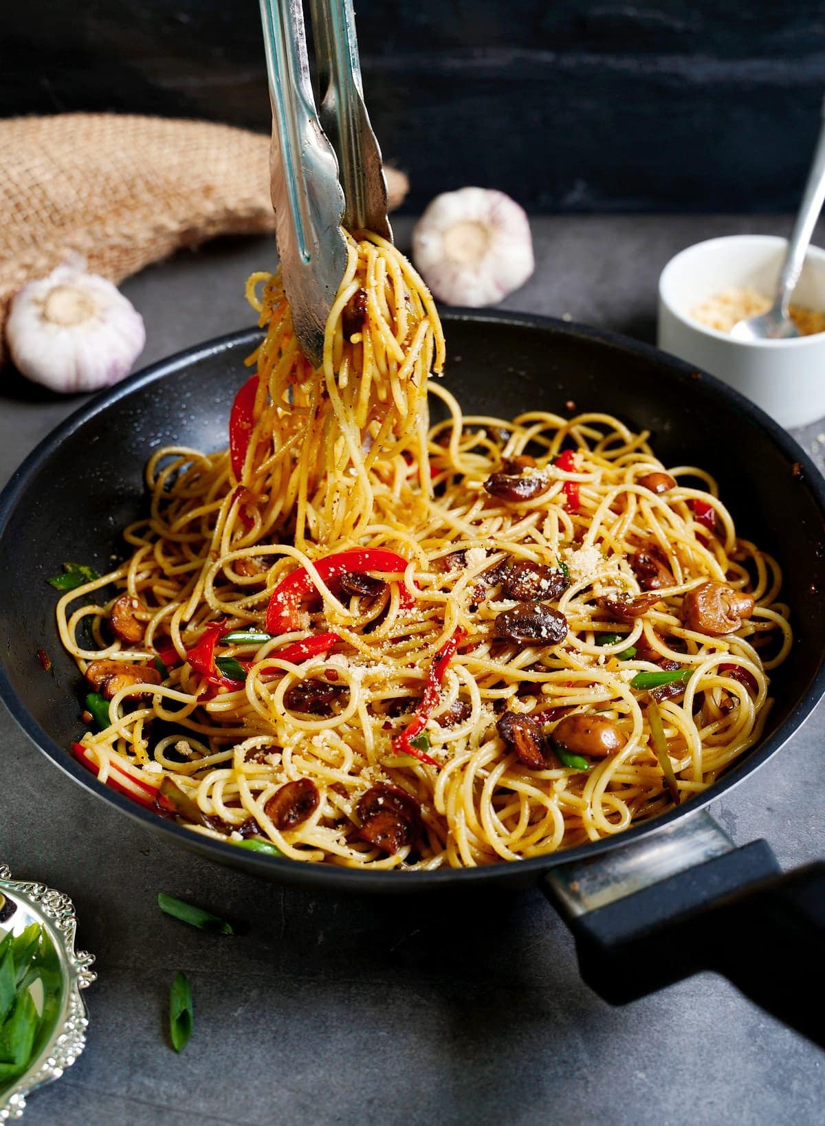garlic noodles in black skillet with veggies and tongs