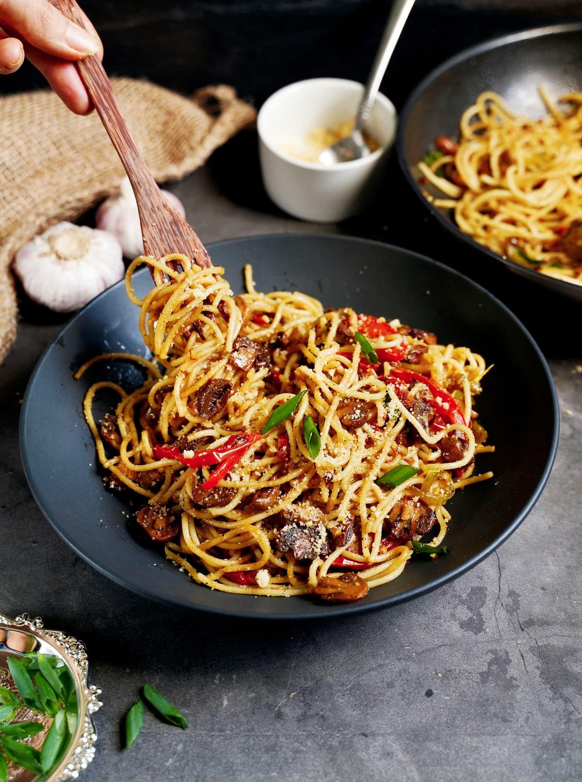 garlic noodles with mushrooms and peppers in black bowl with fork
