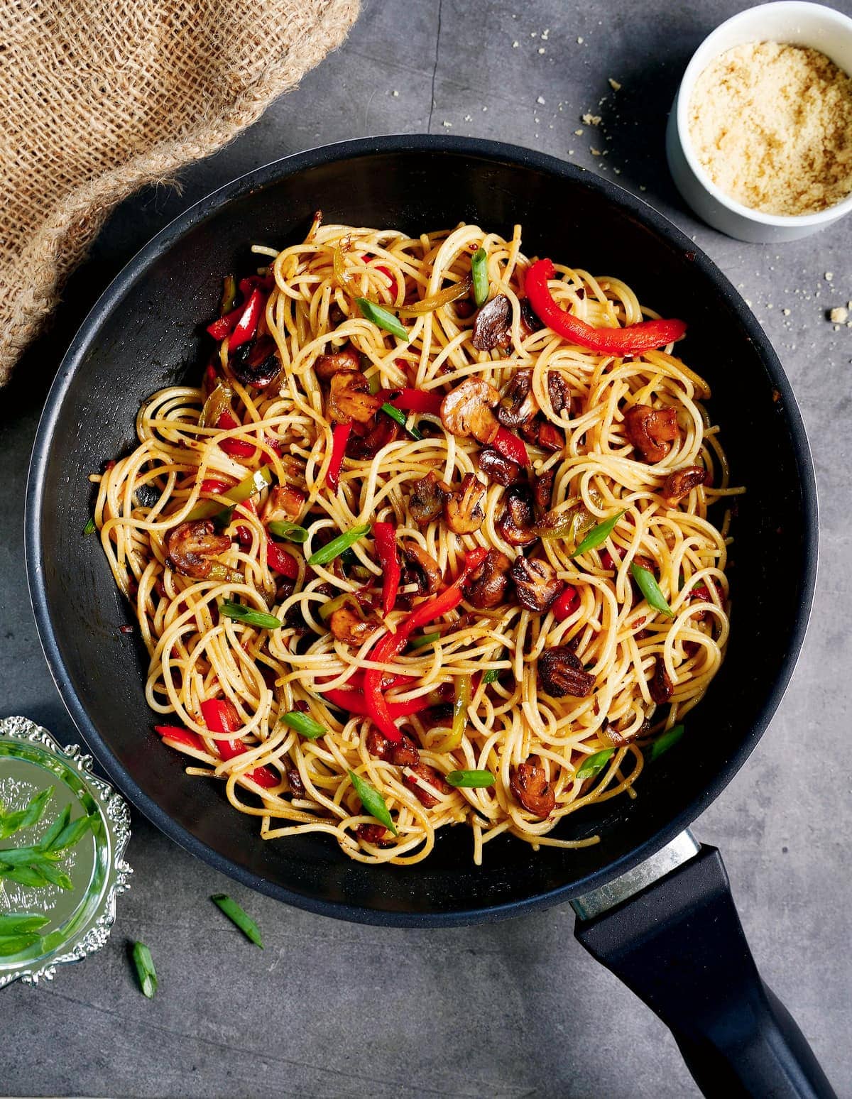 Spaghetti Aglio e Olio in schwarzer Pfanne mit roter Paprika und Champignons von oben