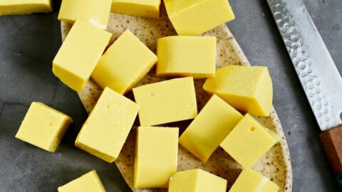 cubed homemade yellow chickpea tofu on ceramic plate with knife on the side