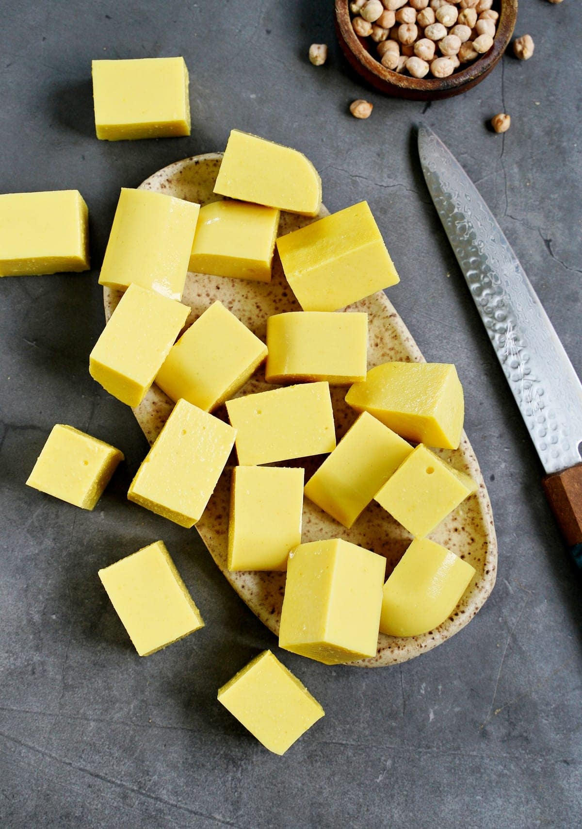 gewürfelter selbstgemachter gelber Kichererbsentofu auf Keramikteller mit Messer an der Seite