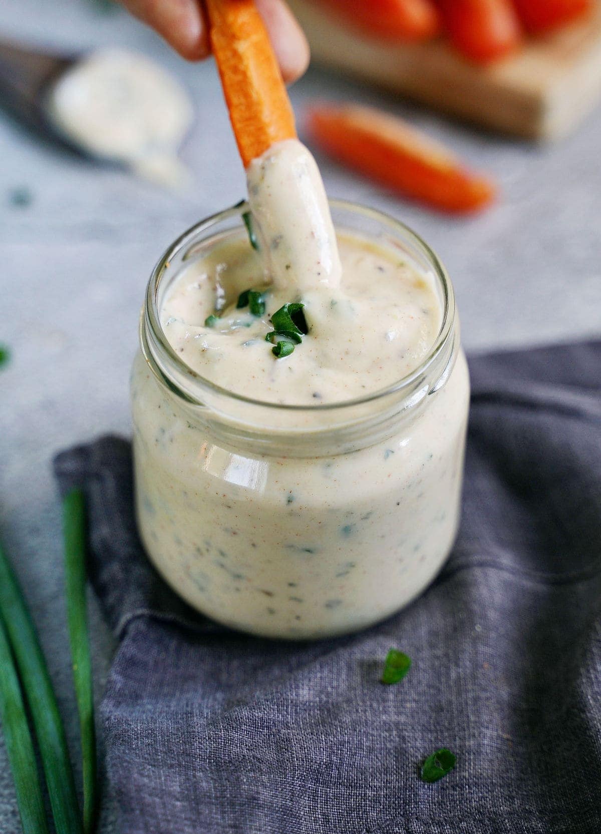dipping carrot stick into ranch dip in glass jar