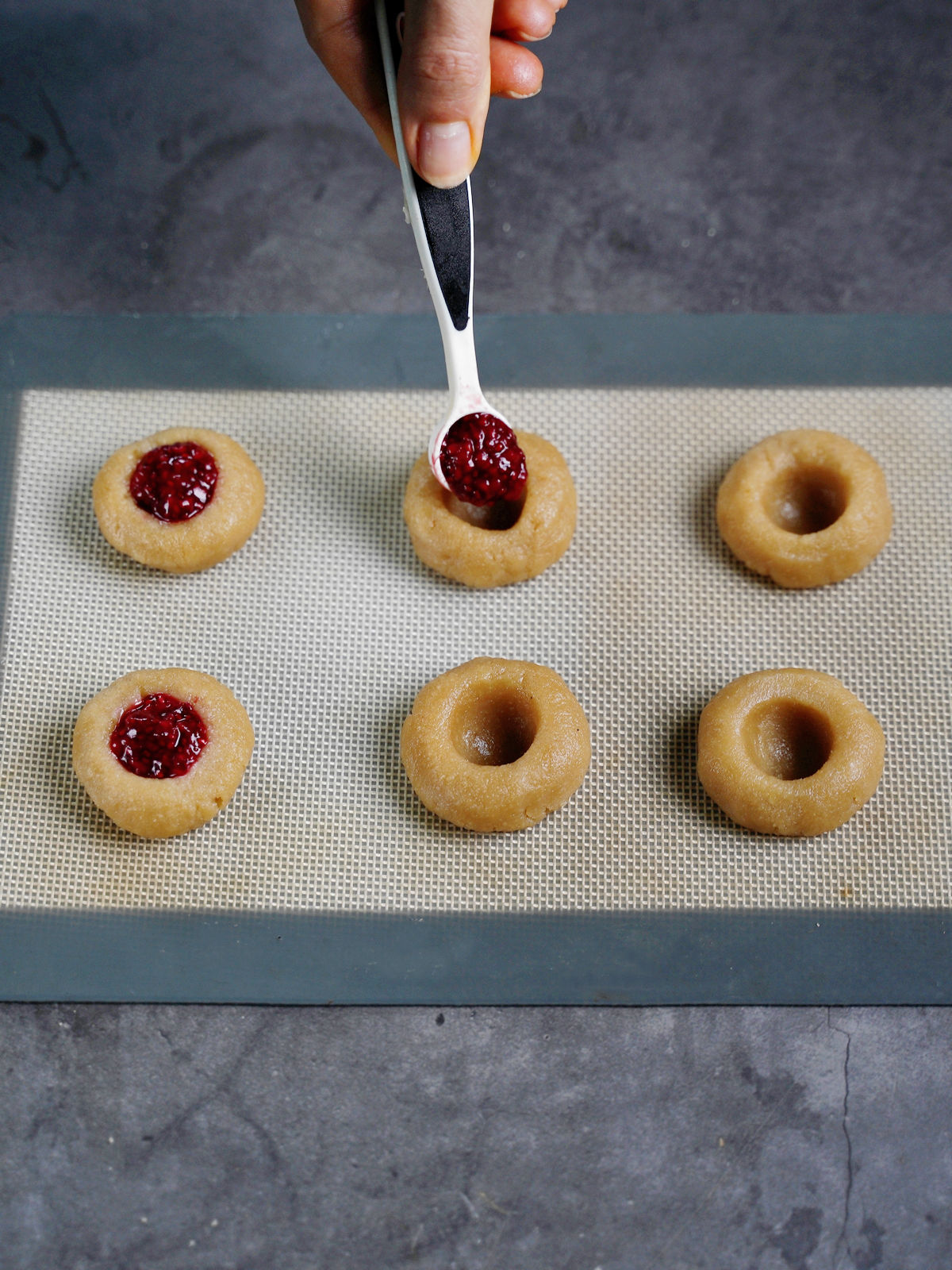 filling raspberry jam into thumbprint cookie