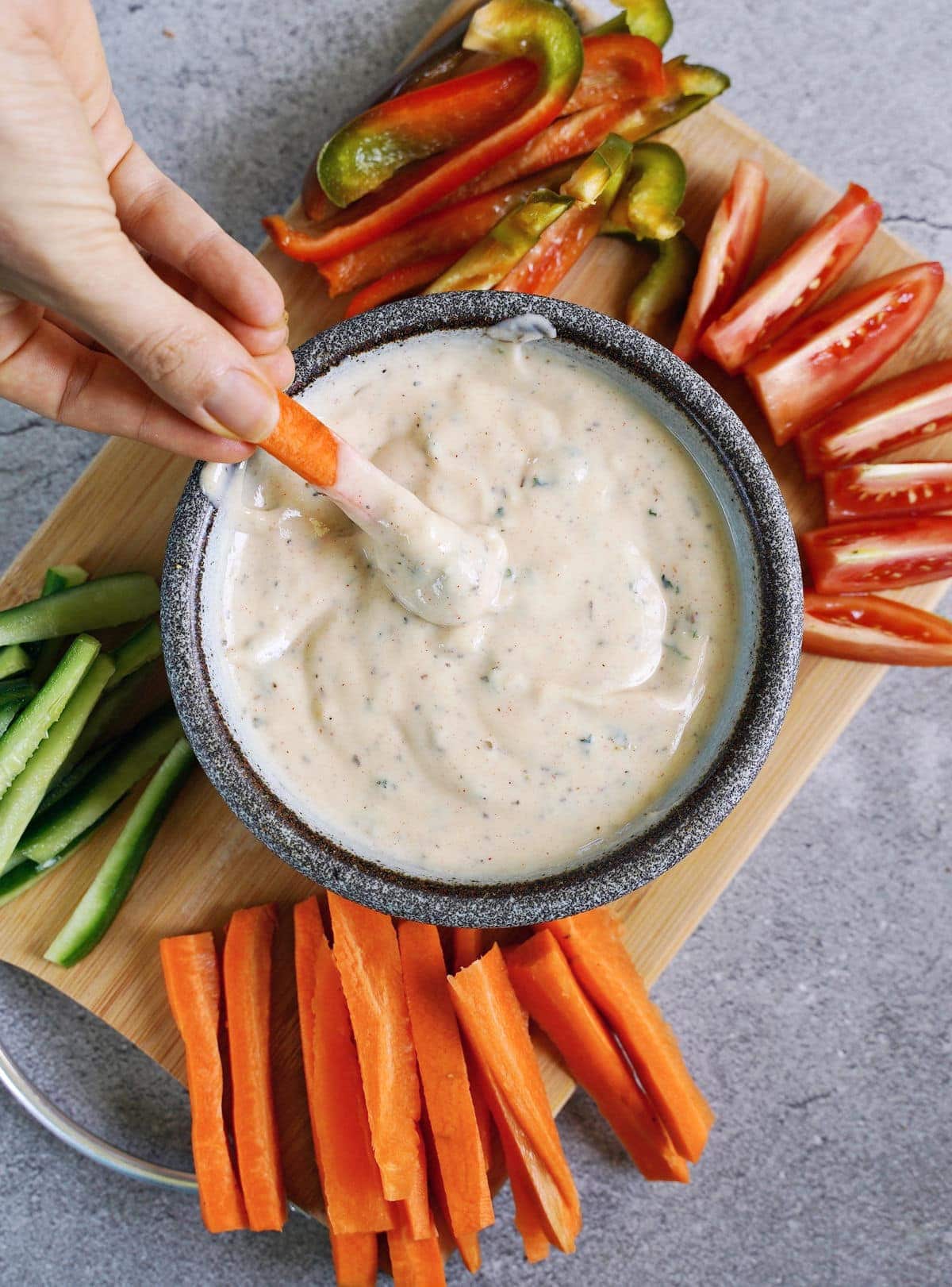 hand dipping carrot stick into vegan Ranch dressing in bowl