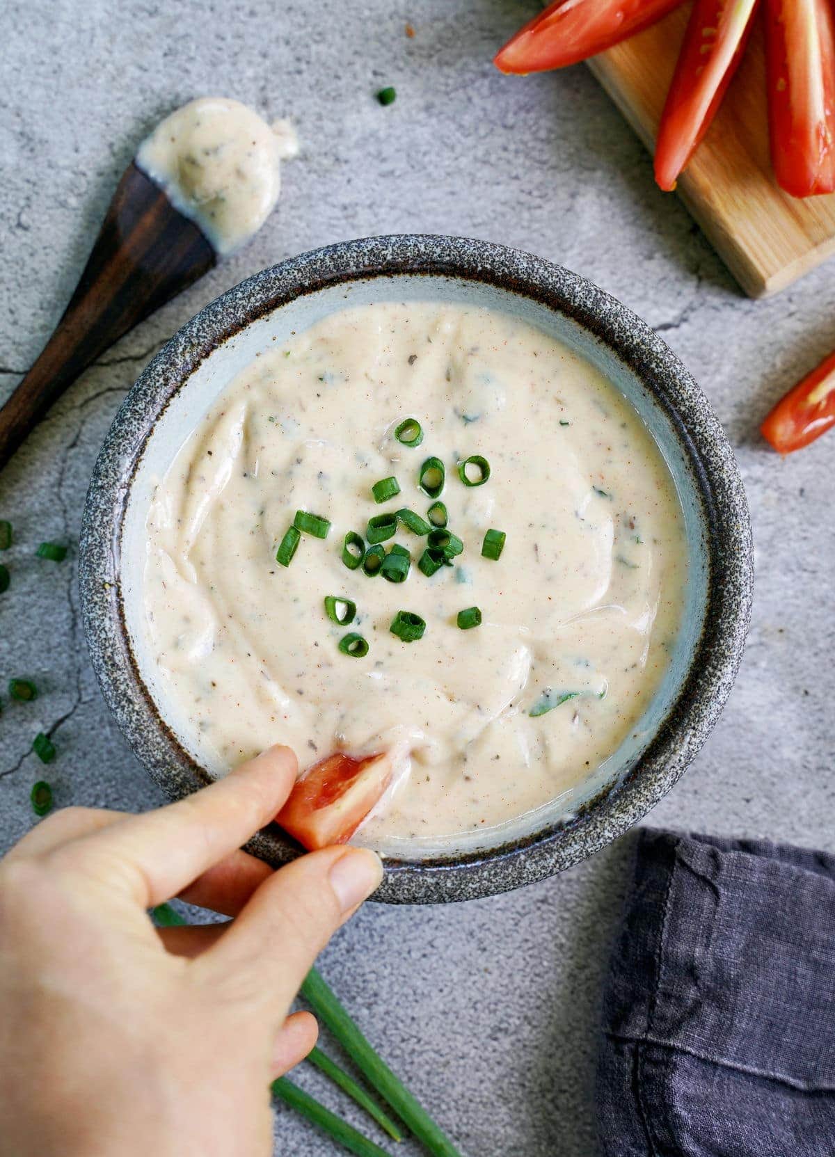 hand dipping tomato slice into bowl with vegan ranch dressing