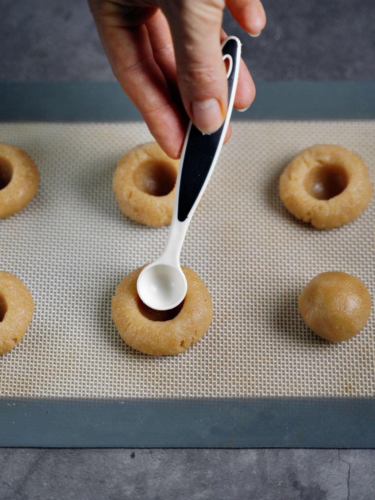 making an indentation to a thumbprint cookie with a measuring spoon