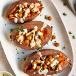 3 baked sweet potatoes on a white plate with roasted chickpeas and white sauce from above