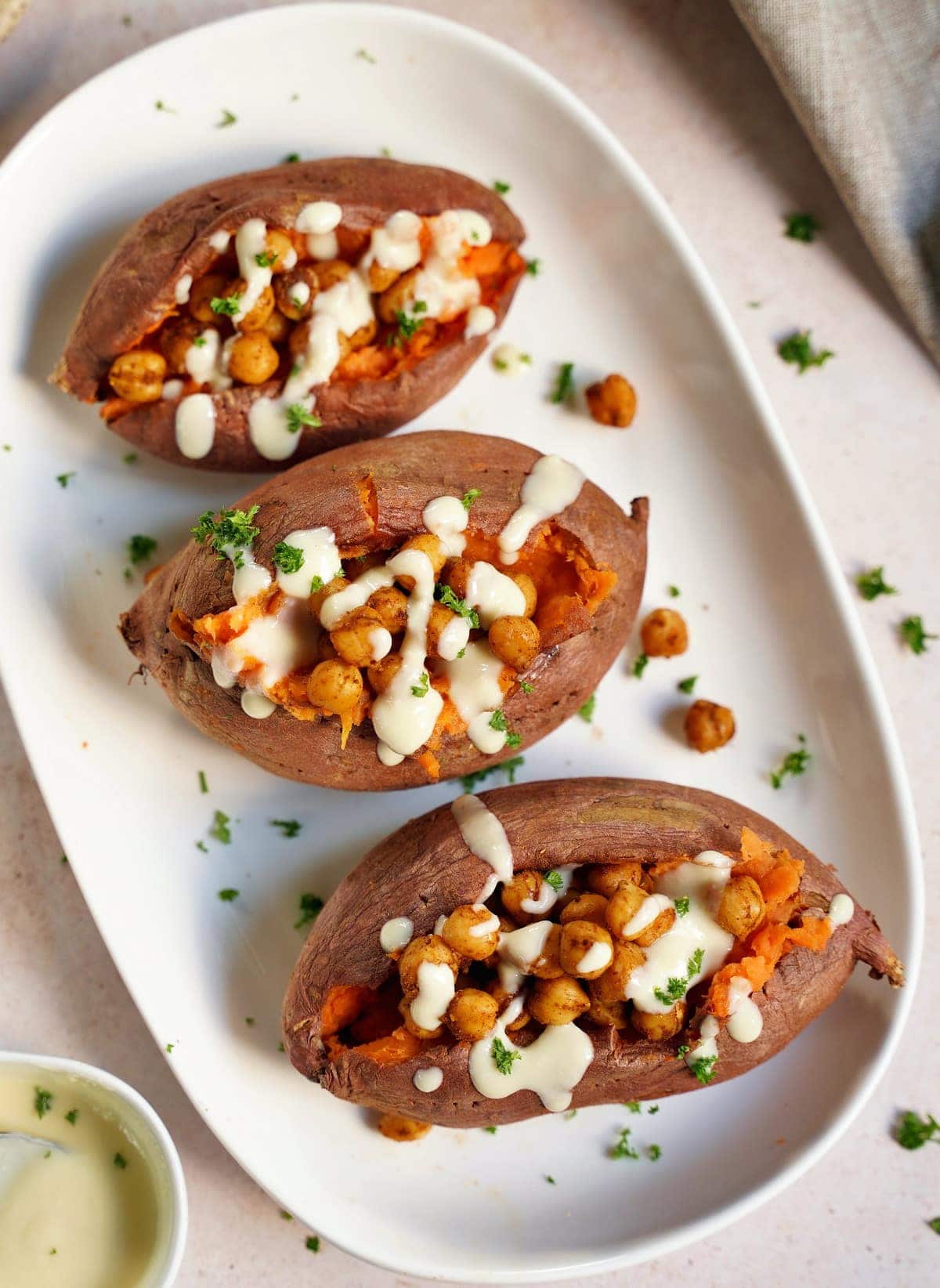 3 baked sweet potatoes on a white plate with roasted chickpeas and white sauce from above