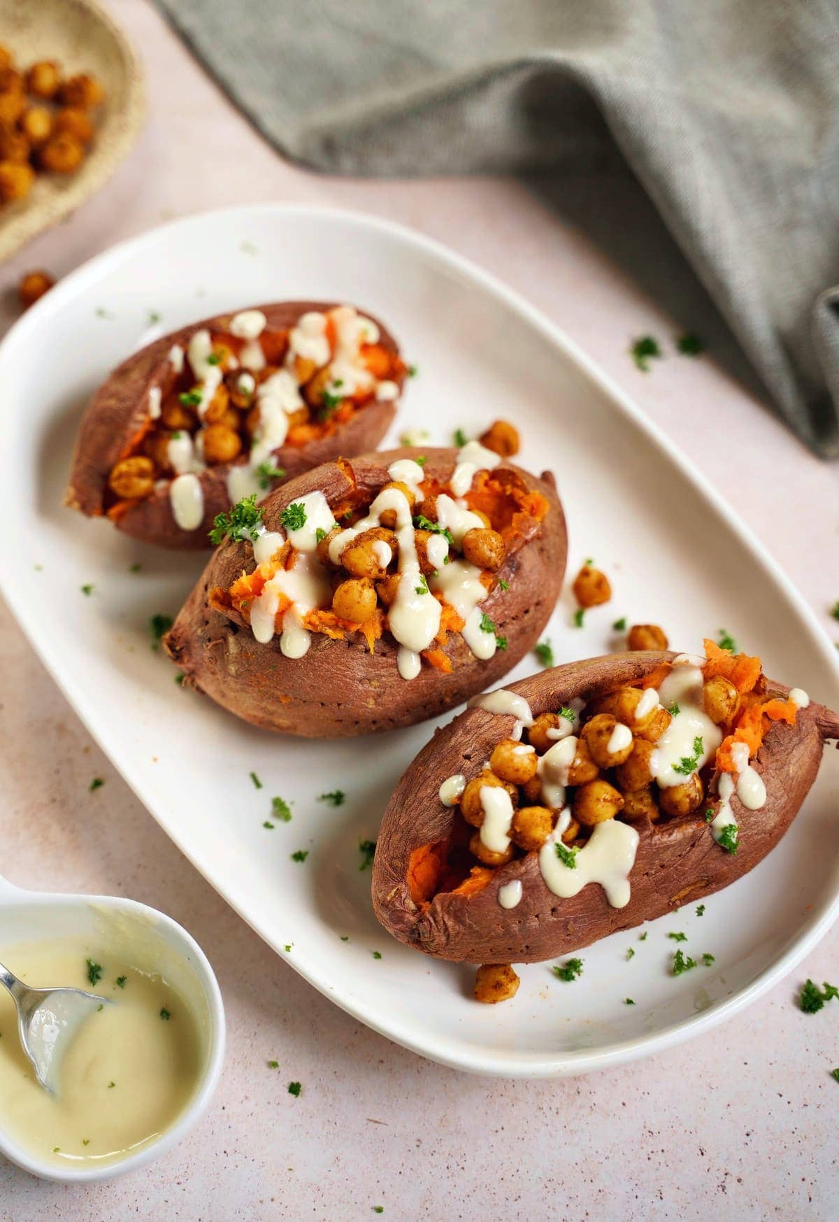 3 baked sweet potatoes on a white plate with roasted chickpeas and white sauce