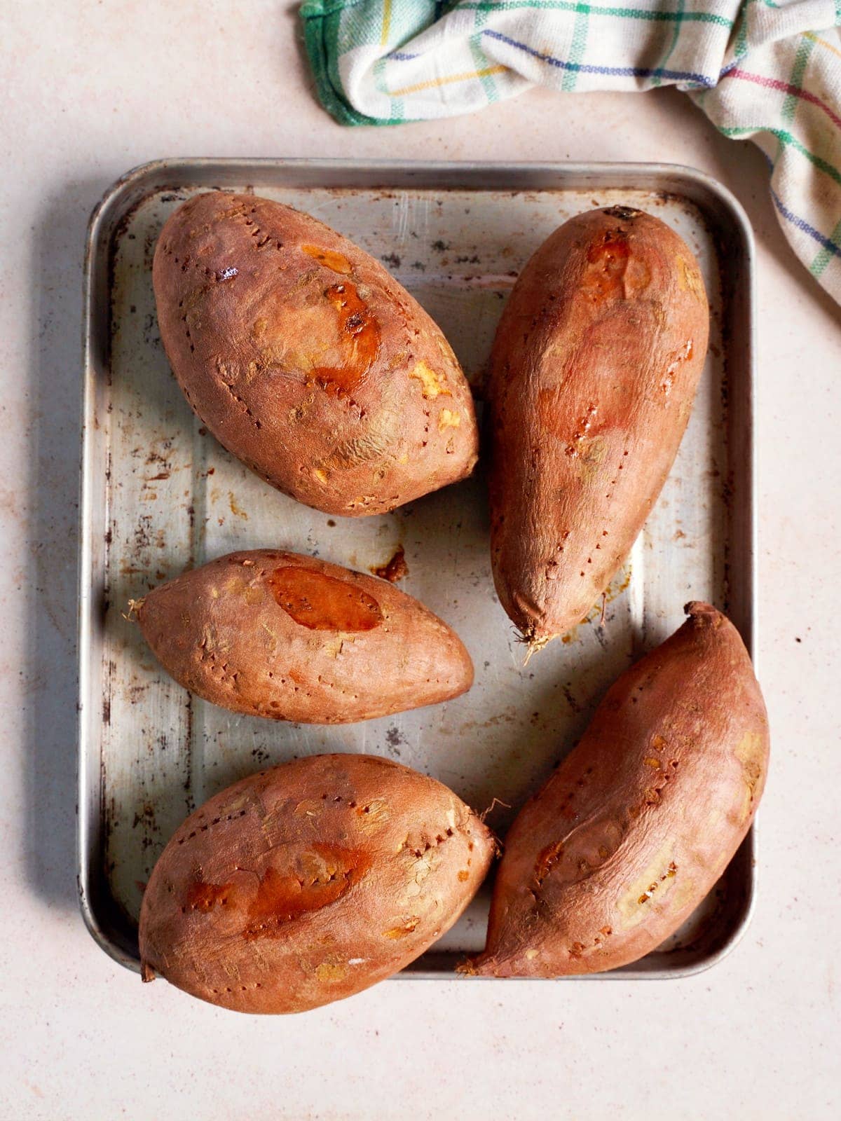 5 baked sweet potatoes on a baking sheet