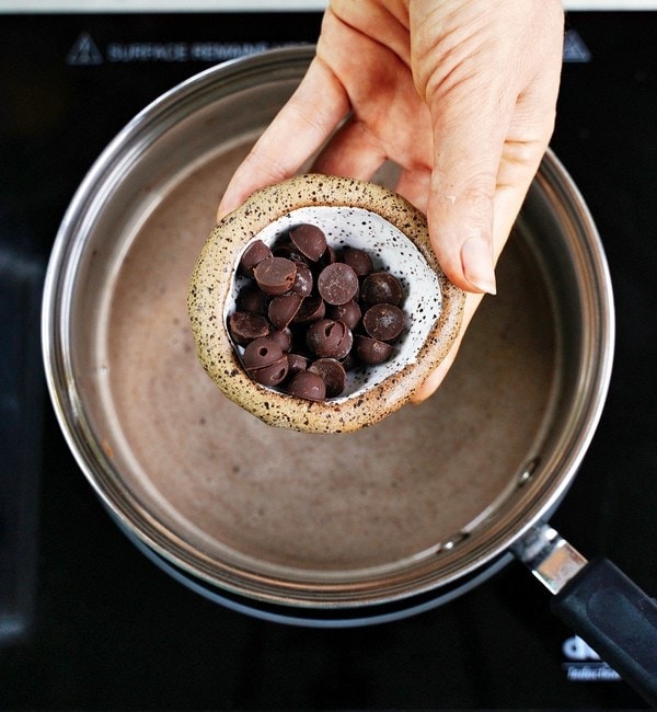 hand holding dairy-free chocolate chips above a saucepan