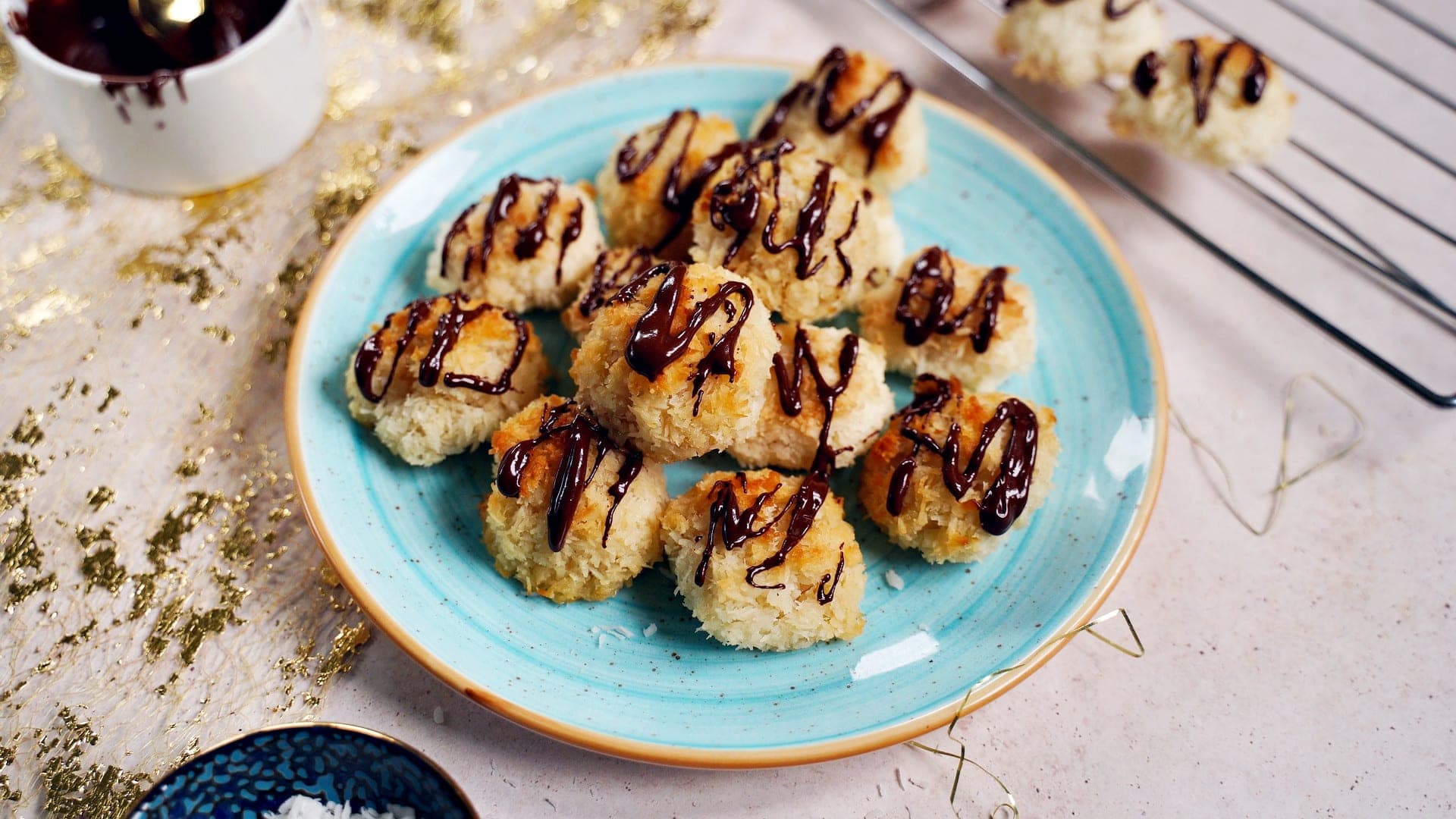 horizontal shot of vegan coconut macaroons drizzled with chocolate on blue plate