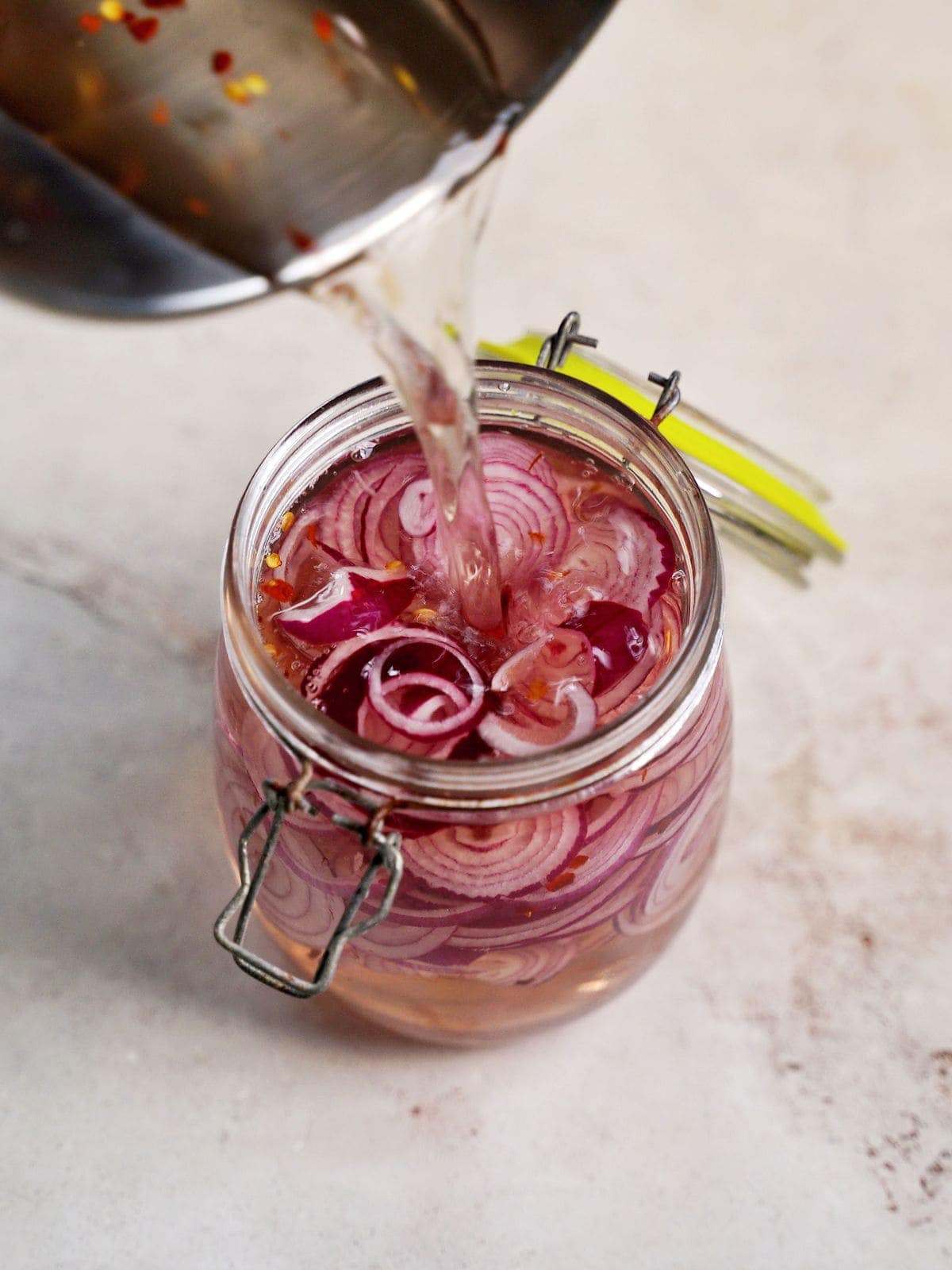 pouring vinegar water into jar with sliced onion