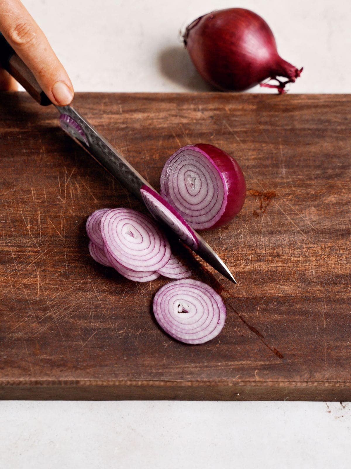 Rote Zwiebel wird mit einem Messer auf einem Holzbrett in Ringe geschnitten