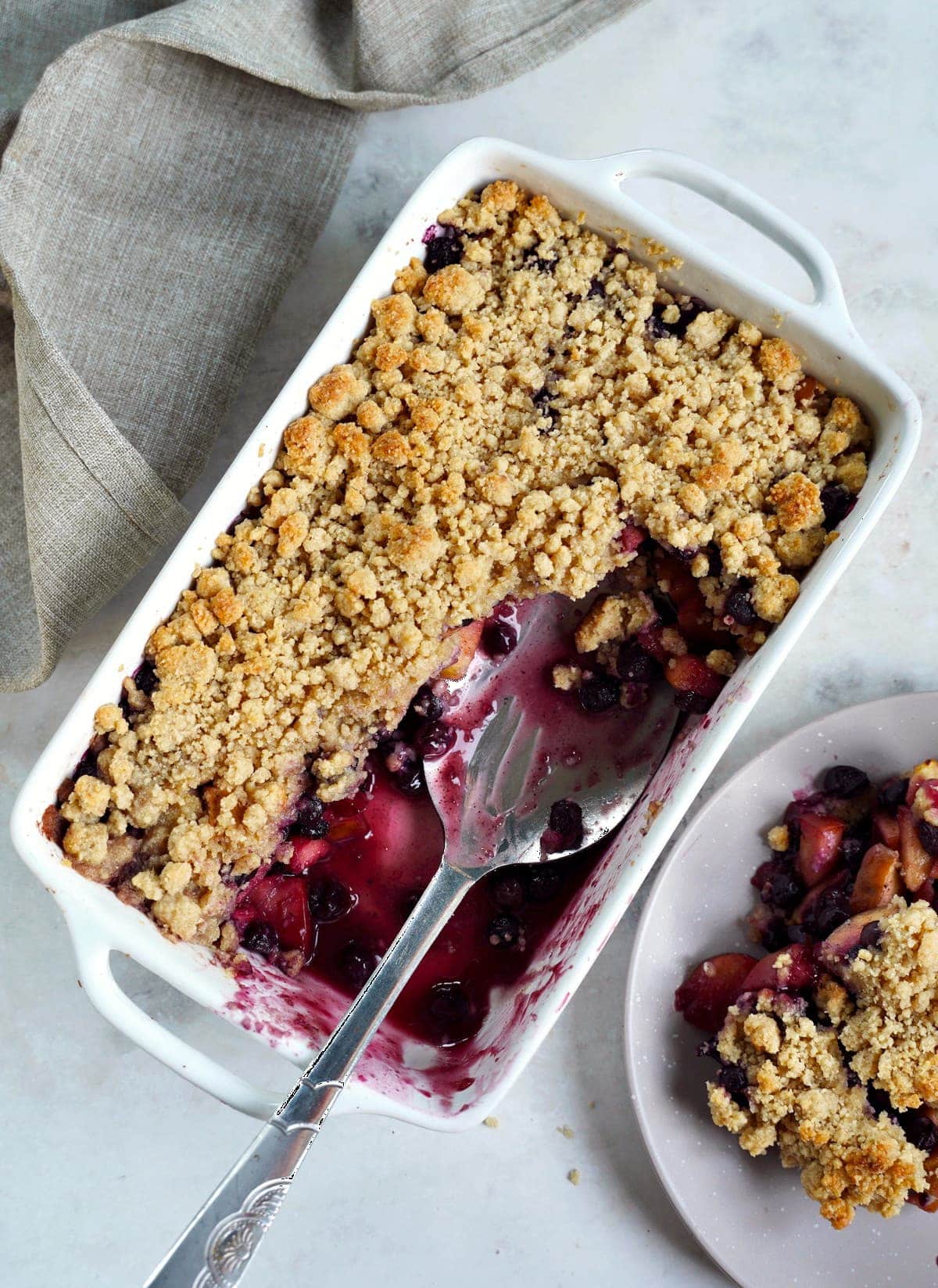 vegan blueberry apple crumble in white pan with large spoon