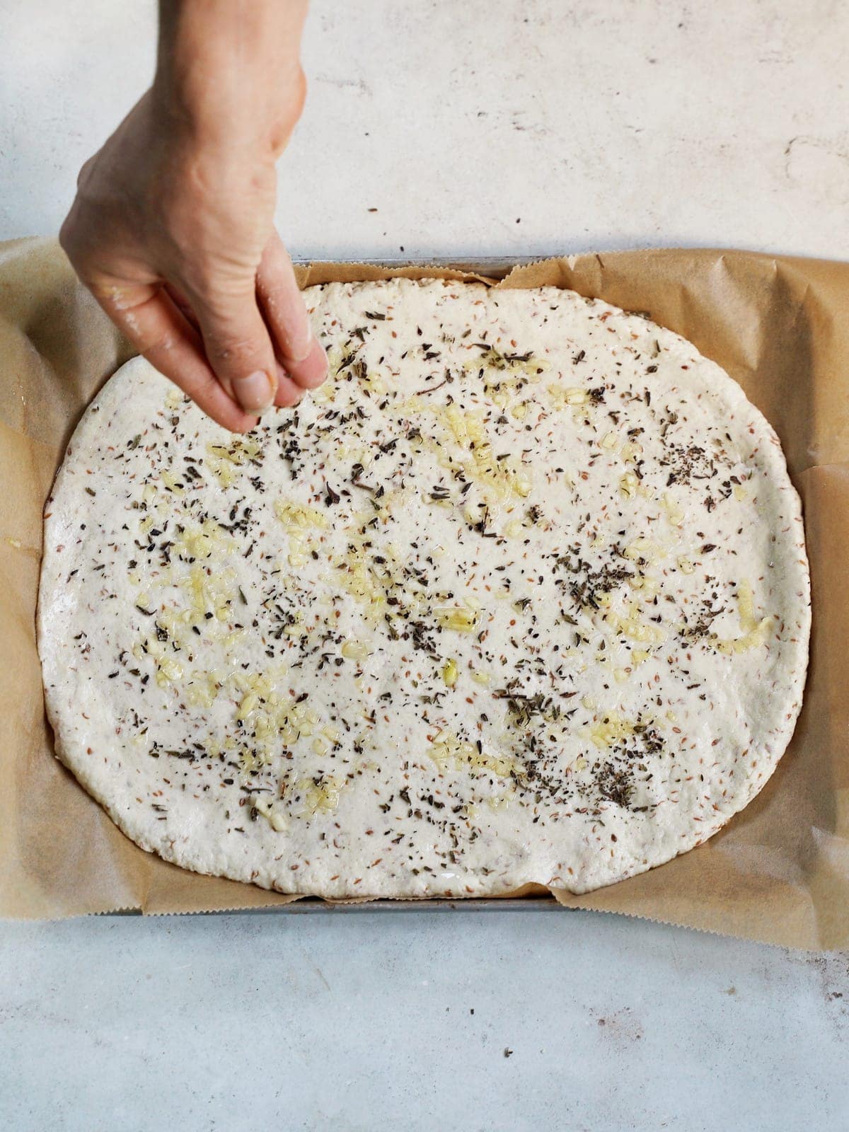 hand sprinkles oregano on pizza dough