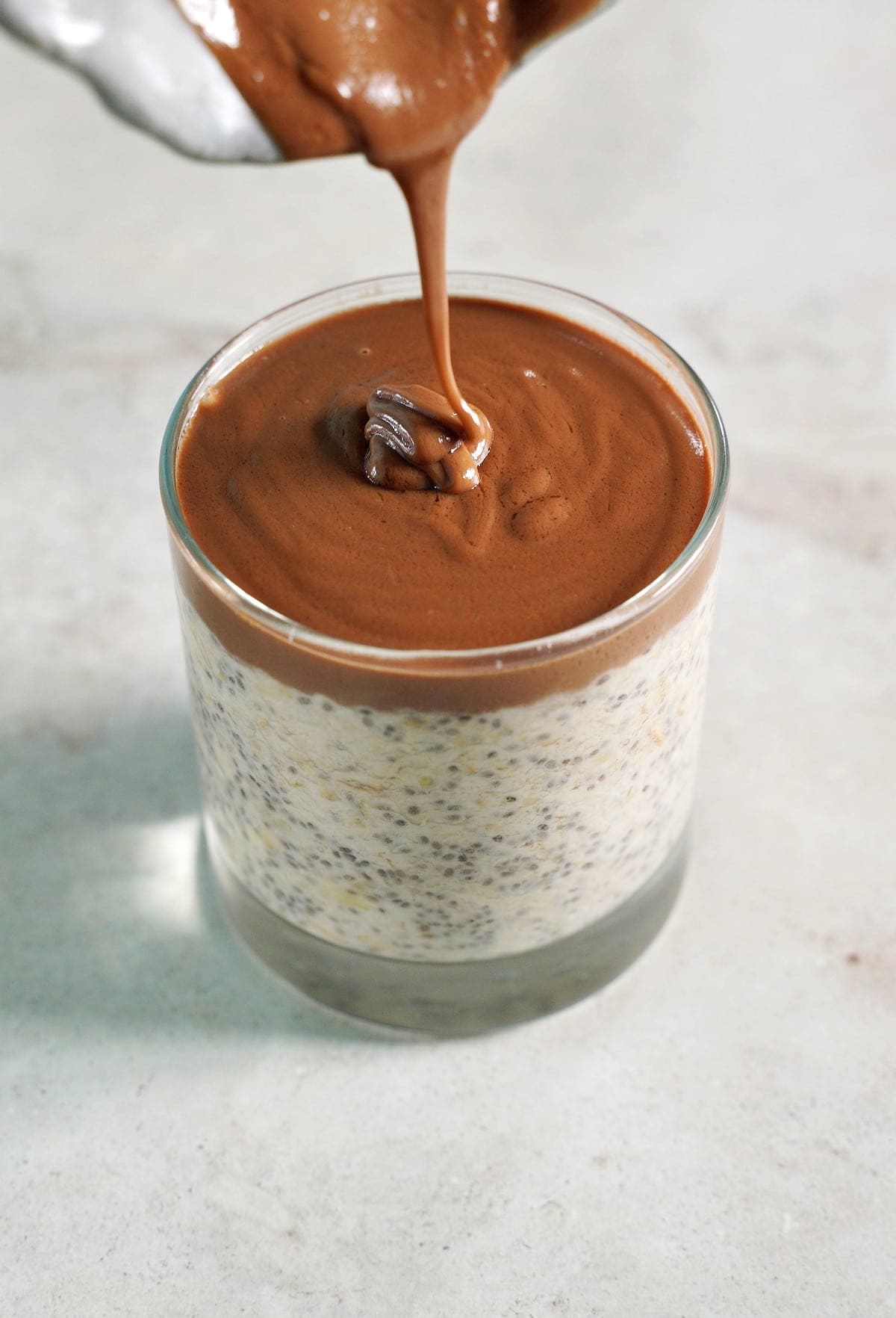 pouring peanut butter chocolate ganache over oat chia mixture in glass