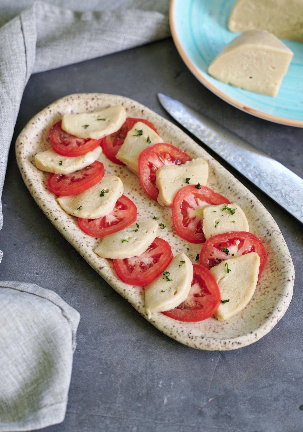in Scheiben geschnittener pflanzlicher Mozzarella mit Tomatenscheiben auf Teller