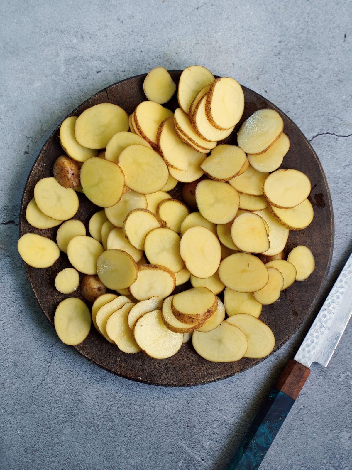 in dünne Scheiben geschnittene Kartoffeln auf einem Holzbrett