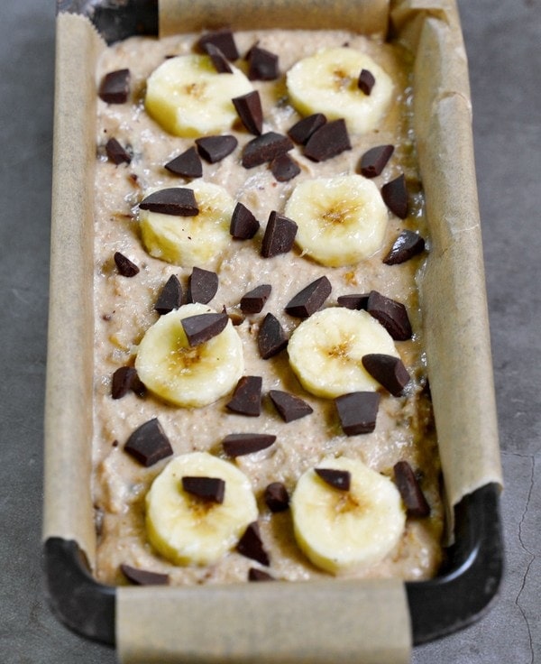 banana bread dough in loaf pan before baking topped with chocolate and sliced banana