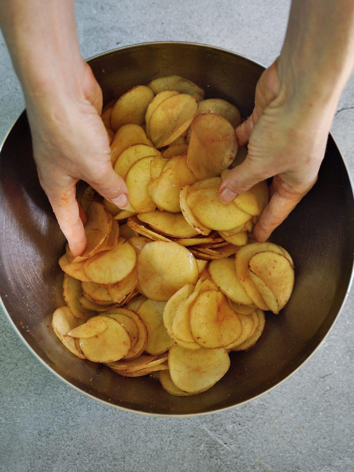 tossing potato slices in silver bowl with hands