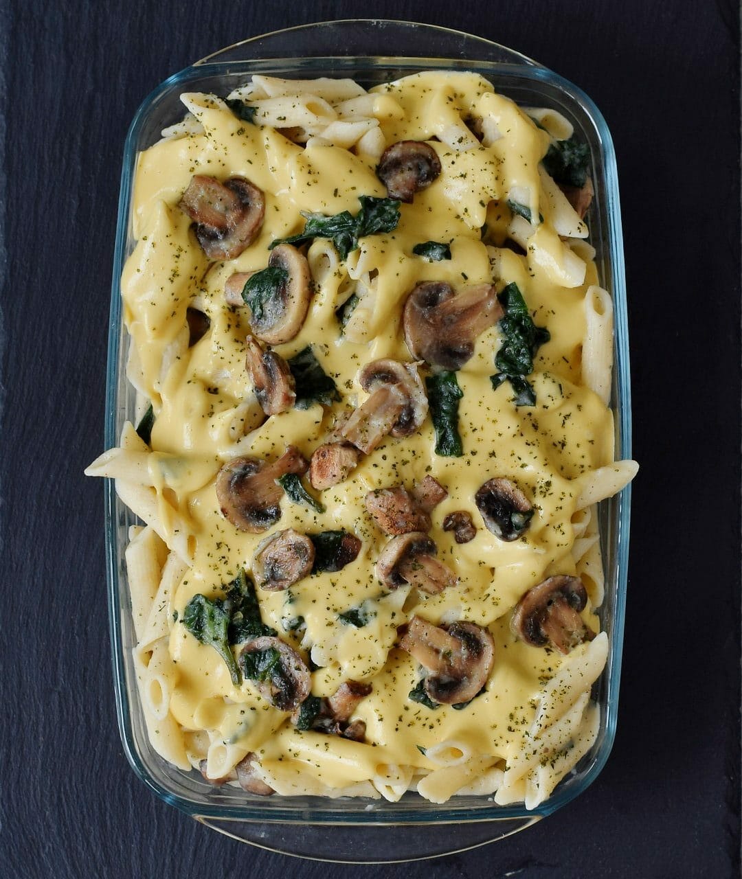 cooked pasta, mushrooms, spinach, and dairy-free cheese sauce in baking dish with creamy sauce before baking