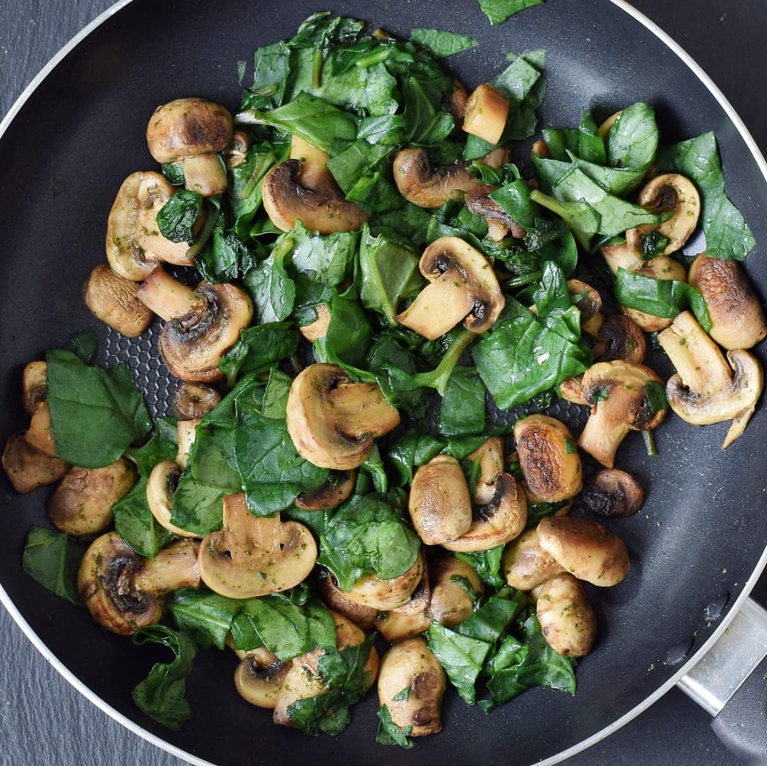 frying mushrooms and spinach in a black skillet